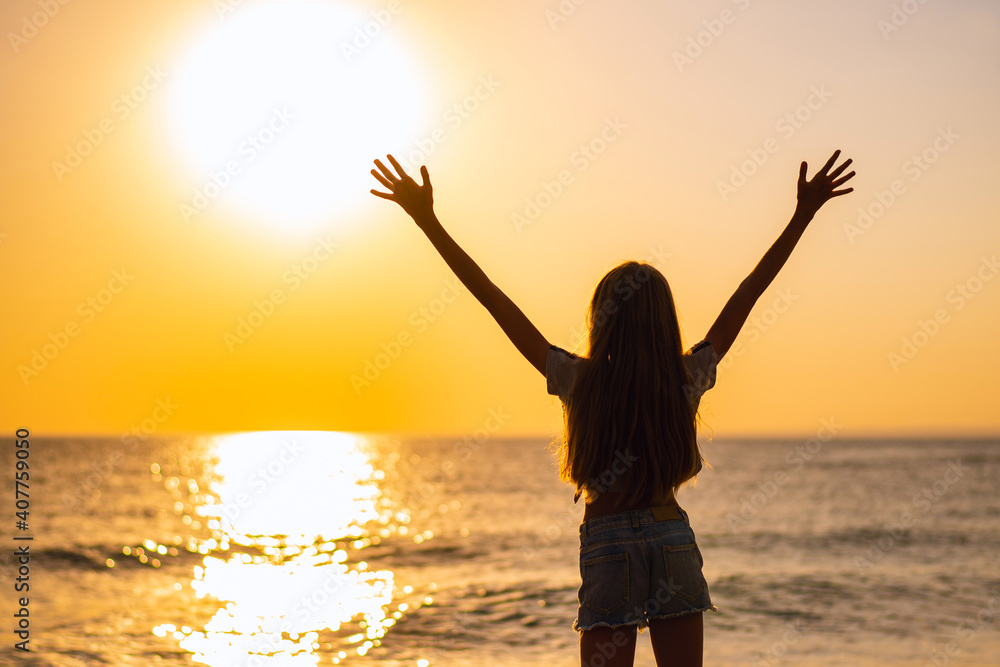 A girl with long hair stands on the seashore with her hands up. girl on looks at a beautiful sunset.