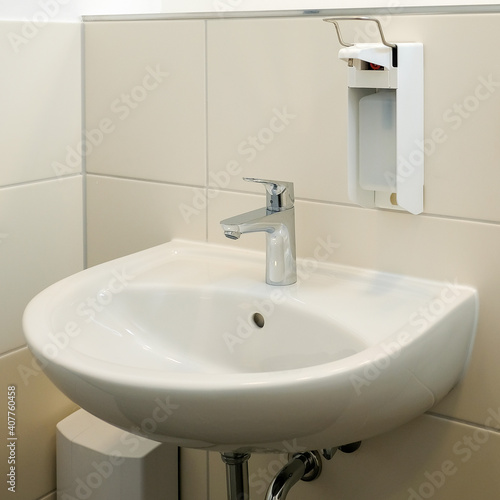 Sink and soap dispenser on a white tiled wall