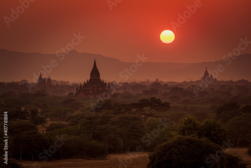 MYAUKI GUNI TEMPLE, SUNSET, TEMPLES OF BAGAN, MYANMAR - 20 January 2016: Sunset across many temple roofs shot in west direction from  Pyathetgyi Pagoda roof top including the sun. photo