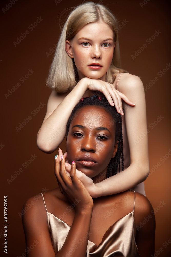 Fototapeta premium two pretty girls african and caucasian blond posing cheerful together on brown background, ethnicity diverse lifestyle people concept