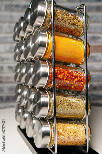 A metal spice rack with many glass bottles filled with different spices