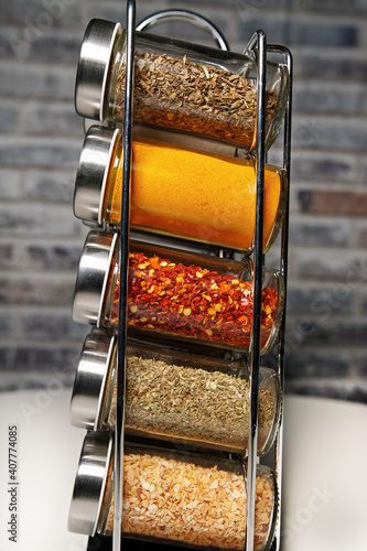 A metal spice rack with many glass bottles filled with different spices