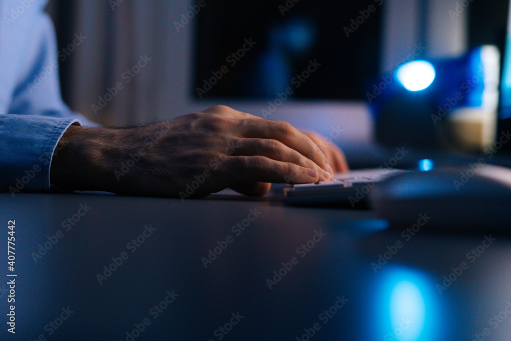 Close-up hands of unrecognizable man writing message to social network. Side view of computer hacker typing code virus pc on wireless keyboard late night working. Concept of remote working.