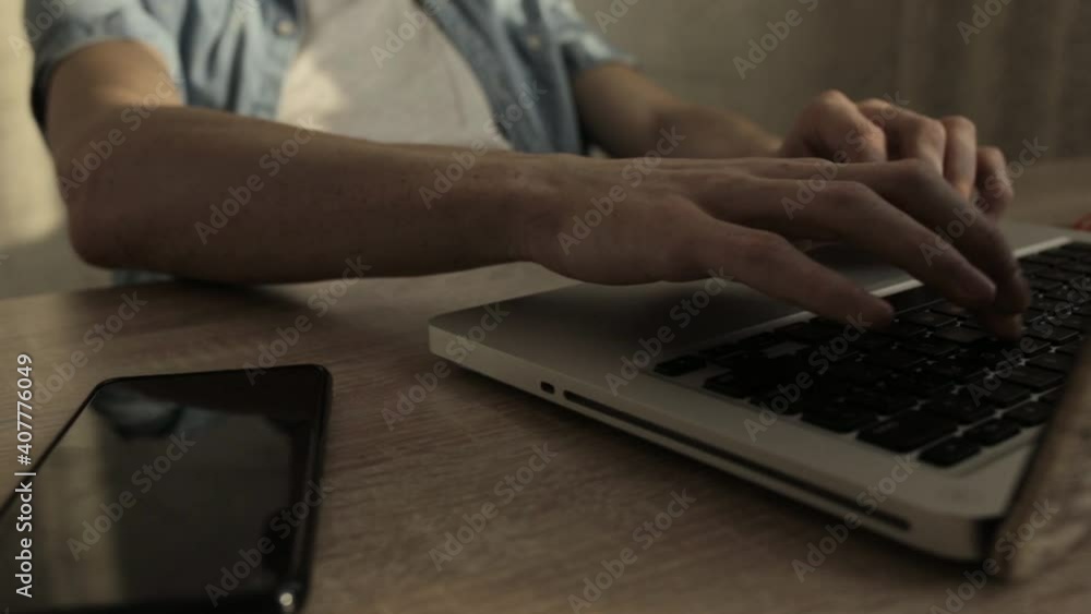 Crop businessman typing on laptop and working remotely on project while sitting at table with smartphone at home Crop businessman typing on laptop and working remotely on project while sitting at table with smartphone at home
