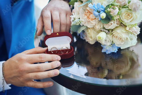 golden wedding rings in a red gift box and a bridal bouquet made of white roses. close-up, macro photo