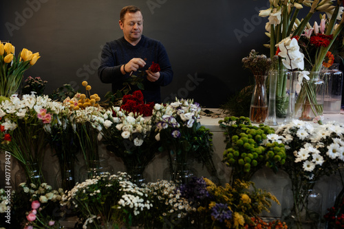 Happy caucasian florist making bouquets of red and pink roses for valentine's day. Concept of human emotions, facial expression, love, and hard work in this pandemic times.