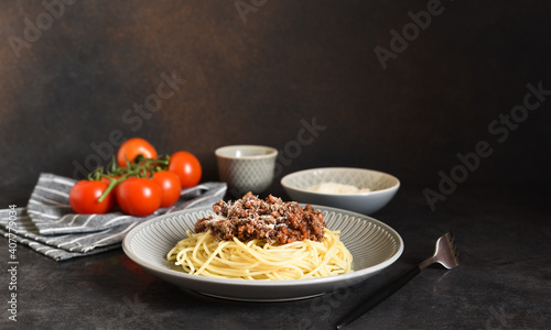 Spaghetti with bolognese sauce, basil and parmesan on a dark concrete background.