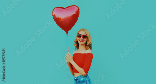 Portrait of cute smiling woman with red heart shaped balloon on a blue background