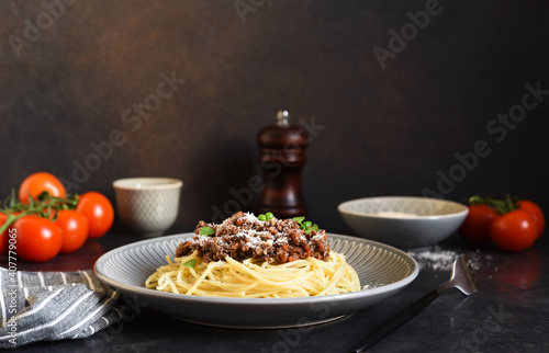 Spaghetti with bolognese sauce, basil and parmesan on a dark concrete background.
