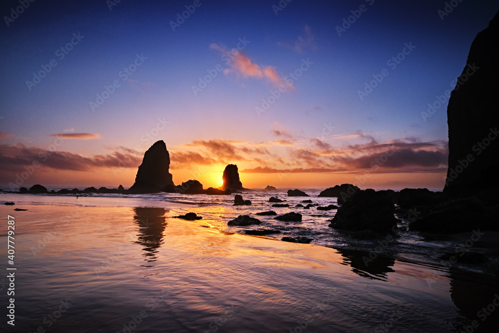Sun about to set behind The Needles as tide pools around Haystack Rock fill with water as the tide comes in