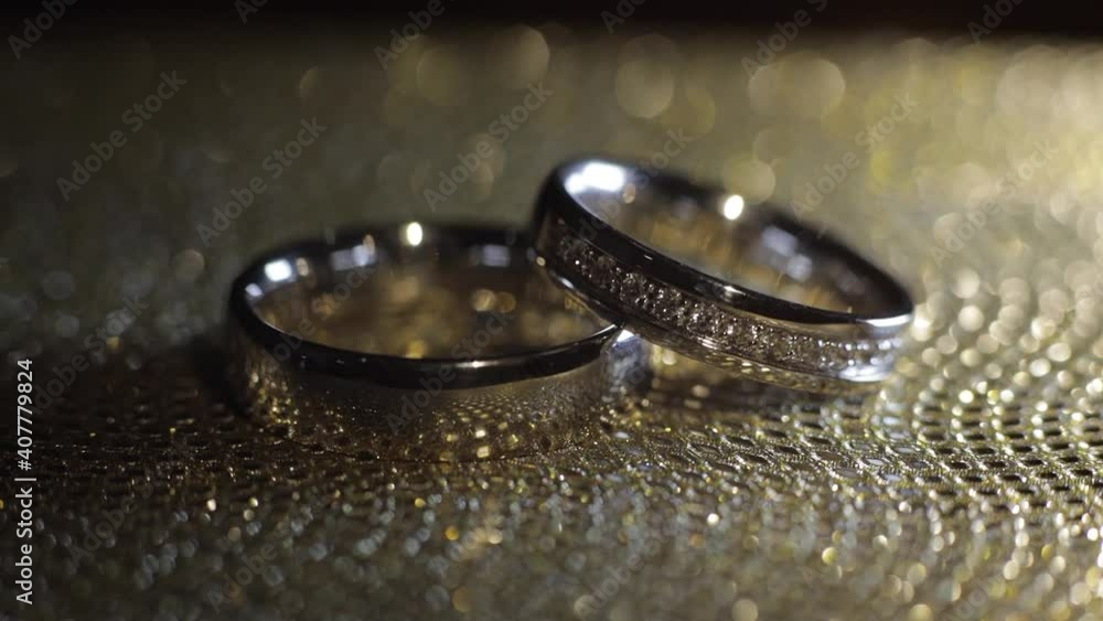 Wedding rings lying on shiny golden shining surface with light, close-up macro footage. Rotate spinning clockwise. Pair of marriage symbols. Love of bride and groom, wife and husband. Matrimony symbol Wedding rings lying on shiny golden shining surface with light, close-up macro footage. Rotate spinning clockwise. Pair of marriage symbols. Love of bride and groom, wife and husband. Matrimony symbol