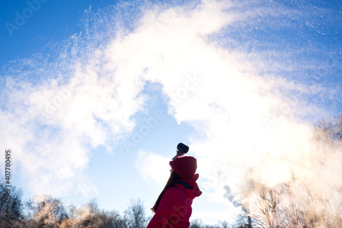 person pouring hot water up in the sky, sunny winter day. Boiling water challenge, which instantly freezes, turns into snow if the temperature is extremely cold