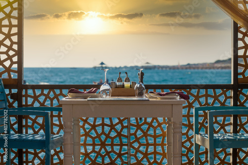 Fototapeta Naklejka Na Ścianę i Meble -  Restaurant with table and two chairs, wine glasses and views of the sea at sunset in Turkey