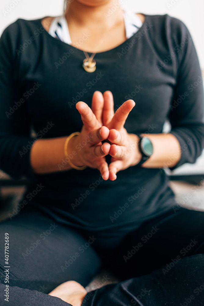 Selective focus of the hands of a Latin woman practicing yoga at home. Vertical picture