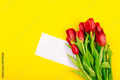 Fototapeta Naklejka Na Ścianę i Meble -  White gift certificate envelope or business card on yellow background with a bouquet of red tulips and copy space, text place. Holiday greeting card. Happy Valentine Day or Woman Day or Mother Day