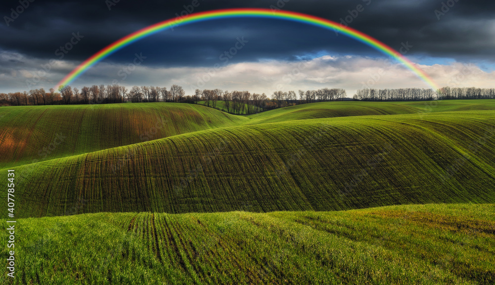  Scenic view of rainbow over green field. dramatic gray sky over a picturesque hilly field 