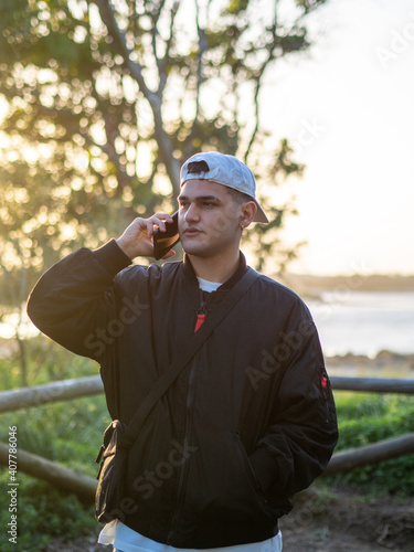 Hombre joven con gorra hablando por teléfono móvil durante la puesta de sol