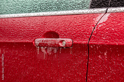 Closeup of car door handle and lock covered in ice during winter storm. Concept of winter driving preparedness and safety