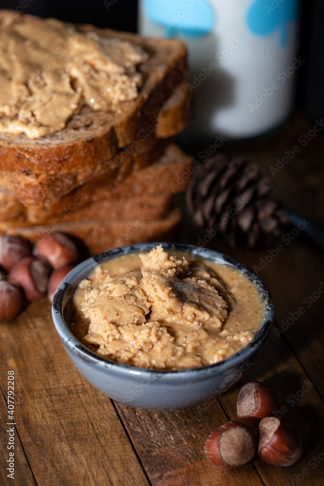 Homemade nut butter in a small bowl. Slices of bread with homemade hazelnut spread and glass of milk on wooden table. Homemade Hazelnut Butter. Homemade nut butter in a small bowl. Slices of bread with homemade hazelnut spread and glass of milk on wooden table. Homemade Hazelnut Butter.