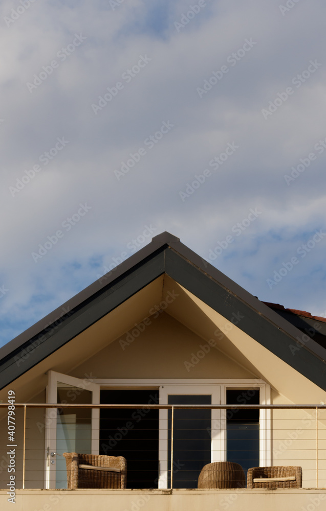 Stylish balcony in a modern suburban house with puffy clouds above. No people. Detail view.