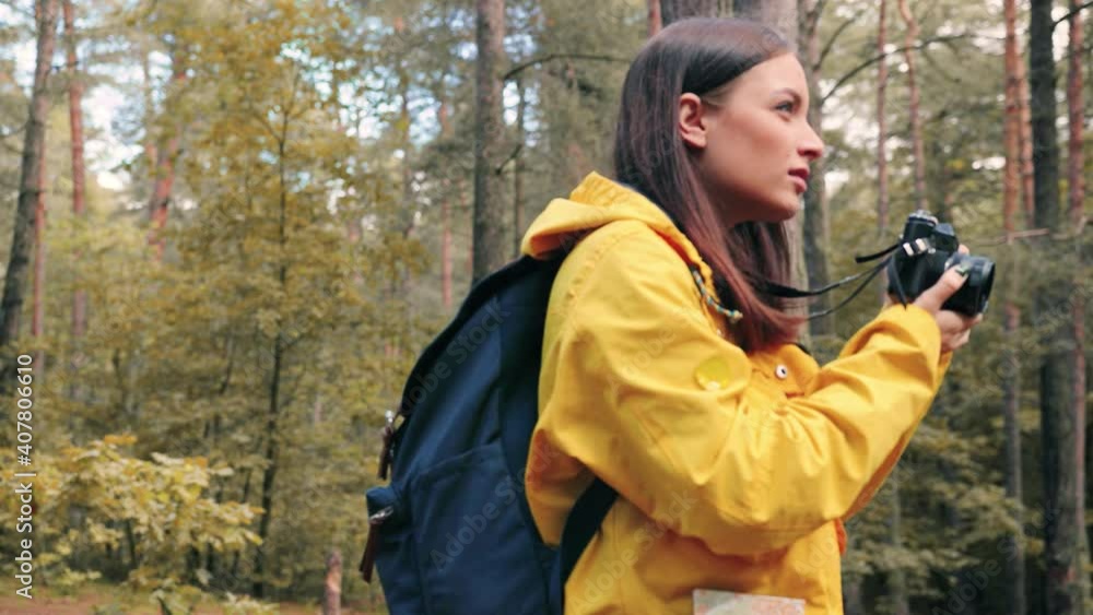 Young beautiful girl tourist in yellow jacket travels alone in woods and takes photos of nature. Caucasian woman is engaged in hobby traveling. Young beautiful girl tourist in yellow jacket travels alone in woods and takes photos of nature. Caucasian woman is engaged in hobby traveling.