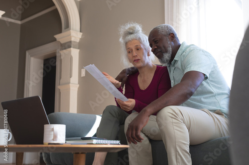 Senior mixed race couple using laptop paying bills together in living room
