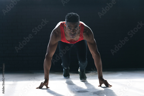 African american man wearing sports clothes kneeling starting to run in empty urban building