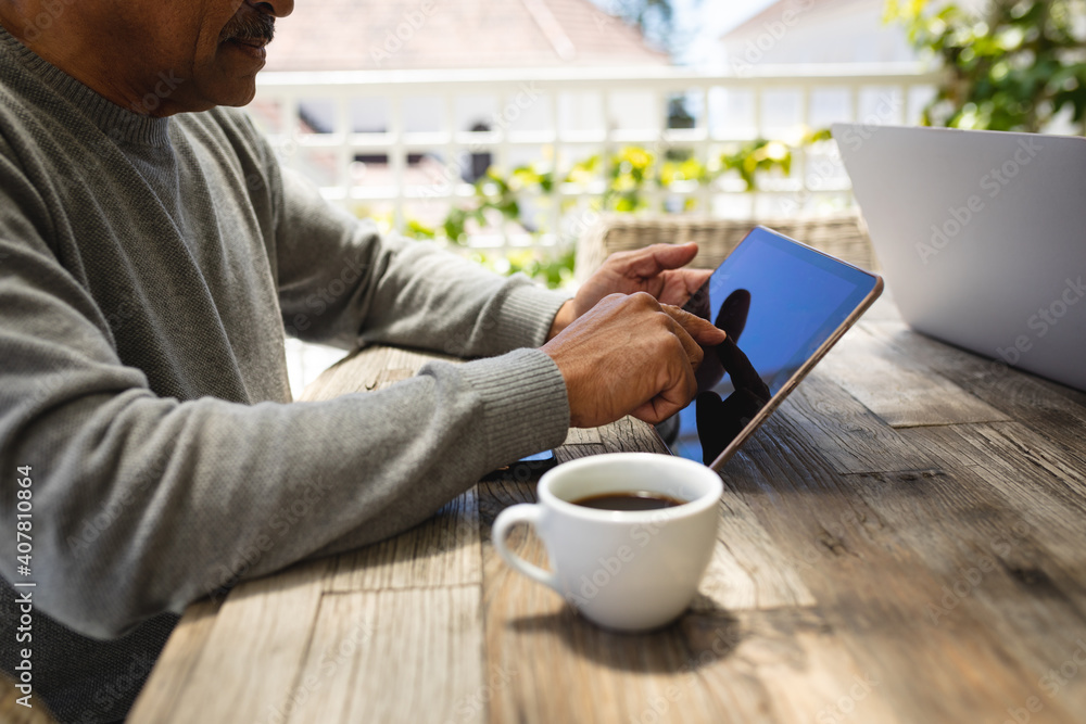 Senior african american man sitting on terrace using digital tablet drinking coffee Senior african american man sitting on terrace using digital tablet drinking coffee