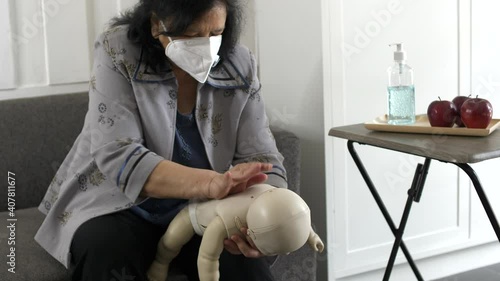 A woman practicing Heimlich maneuver on an infant mannequin by delivering sharp short blows to the surface of the back of the model. photo