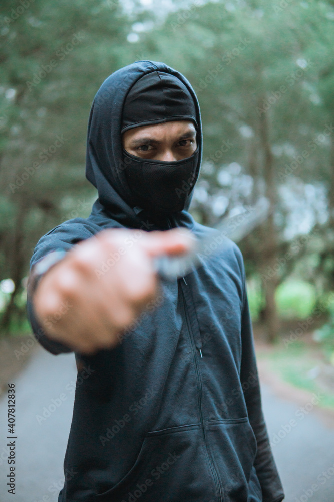 close up of thief in a mask with a knife wearing black hoodie pointed the knife at the camera when stand on the road close up of thief in a mask with a knife wearing black hoodie pointed the knife at the camera when stand on the road