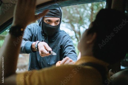 Bandit man with masked robber holding knife to hijack hostage man driver car shocked and dangerous on street violence concept