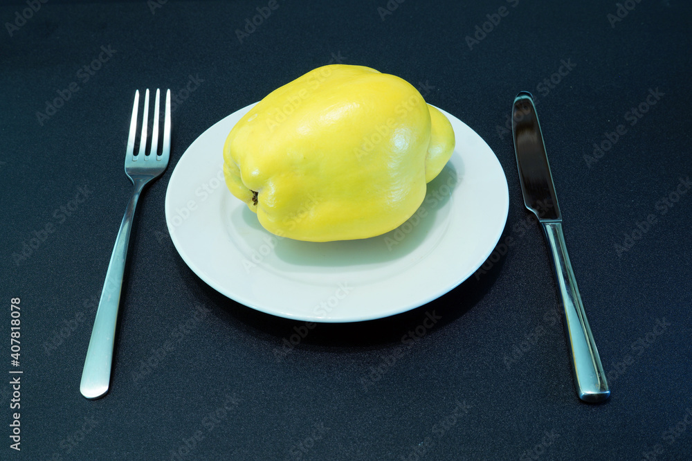 Large quince fruit on a white plate on a black table. Raw vegetarian food. Large quince fruit on a white plate on a black table. Raw vegetarian food.