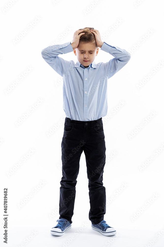 Fototapeta premium A schoolboy stands and holds his head with his hands. White background. Vertical.