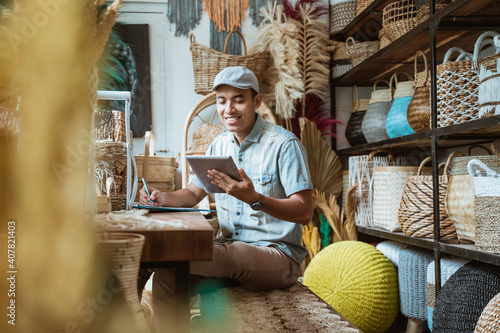 The shop owner notes with a pen while using a digital tablet while sitting in a craft store