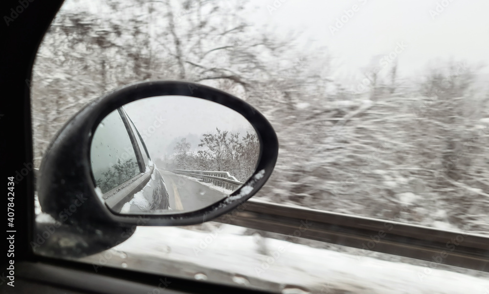 Winter. Reflection in the side mirror of the car. Beautiful winter landscape with snowy fir trees in car rear view mirror. Winter travelling concept Winter. Reflection in the side mirror of the car. Beautiful winter landscape with snowy fir trees in car rear view mirror. Winter travelling concept