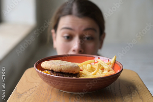 Young woman tempted by junk fast food and takes fries from plate