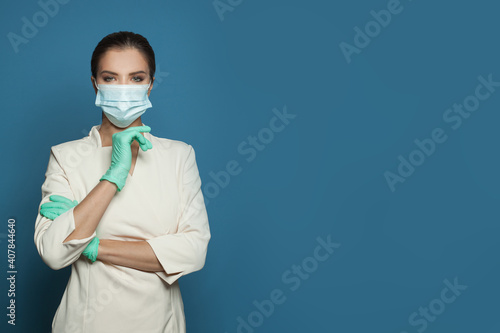 Doctor in protective medical mask and nitrile surgical gloves on blue background, medicine, safety and virus protection concept