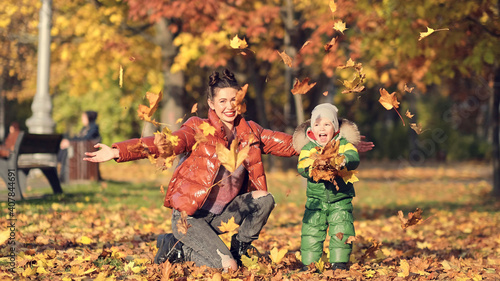 Mom and son throw autumn leaves in autumn park, family fun. family enjoying a walk in nature. happy motherhood concept.