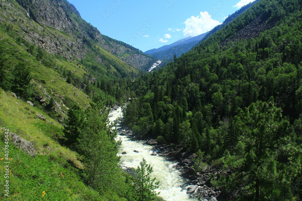 Altay waterfall Uchar in summer.The river is high in the mountains on a summer day,on the banks of the river there are stones, on the mountains a forest grows, the slopes of the mountains are rocky