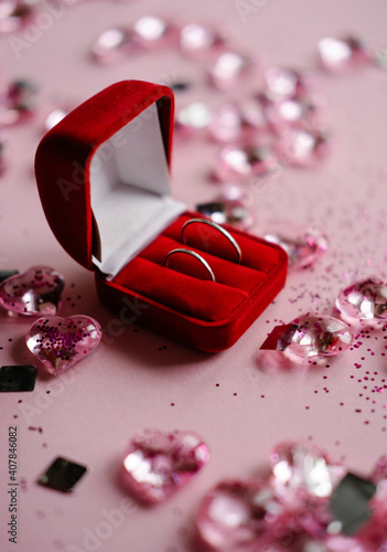 wedding rings in a red box on a pink background with hearts and silver confetti. vertical photo on Valentines day
