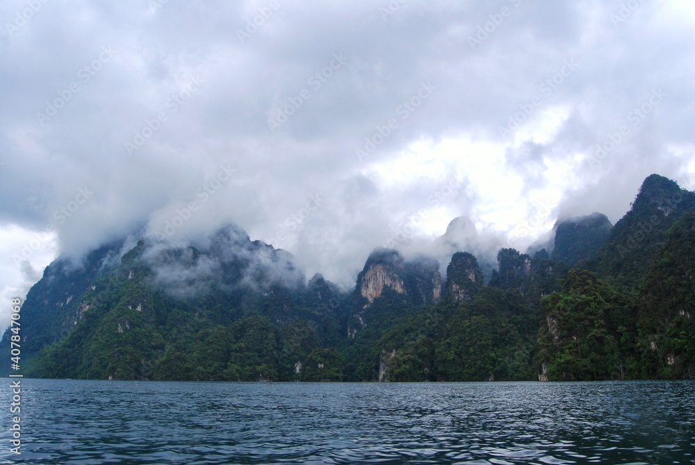 Mountain view with tropical rainforest behind and Blue Water Lake at Ratchaprapha dam or Khao Sok National Park, Surat Thani, Thailand.