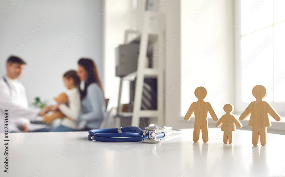 Stethoscope with small wooden mom, dad and kid figures standing on doctor's table at clinic or hospital. Medicine, family health care and regular checkup concept. Blurred background for medical text