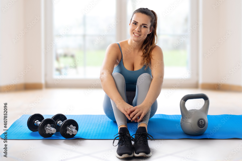 Fototapeta premium Young woman sitting on yoga mat during home workout