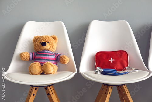 Cute teddy bear, first-aid kit and stethoscope on two white chairs in children's medical center or pediatric clinic waiting room. Kids' visit to hospital to see pediatrician or family doctor concept photo
