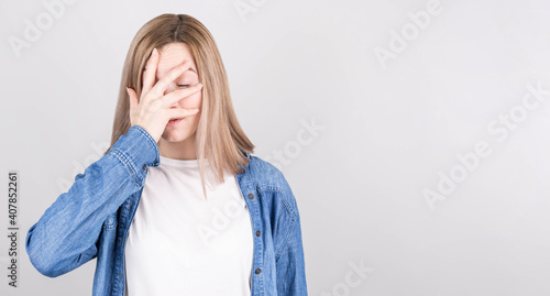 Obraz na plátně Portrait of an unlucky girl in a denim shirt, standing with a facepalm gesture, feeling regret and sadness, blaming herself for a mistake, disappointed in defeat