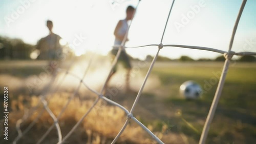 The brothers play football on the old field in the rays of the sunset. Local boys kick the ball. Football concept. Street sports in a poor area of a city or village. Training. Childhood memories.	