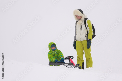 Mom and son sledding from the mountain in winter in heavy snow