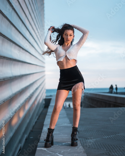 Posing of a pretty brunette girl in the city at blue hour next to a gray building  wearing black boots and a short black skirt