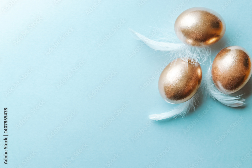 Golden easter colour eggs with white feathers on pastel blue background in Happy Easter decoration. Spring holiday top view concept. Golden easter colour eggs with white feathers on pastel blue background in Happy Easter decoration. Spring holiday top view concept.