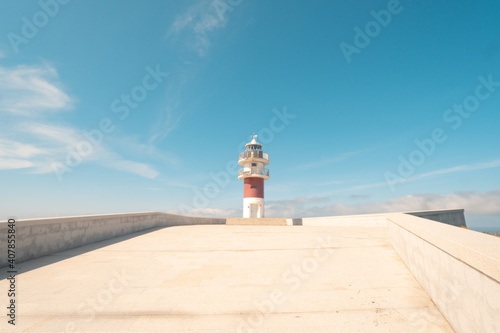 White and red striped lighthouse, with a blue sky with some cloud. In Cabo Ortegal, Galicia, northern Spain. photo